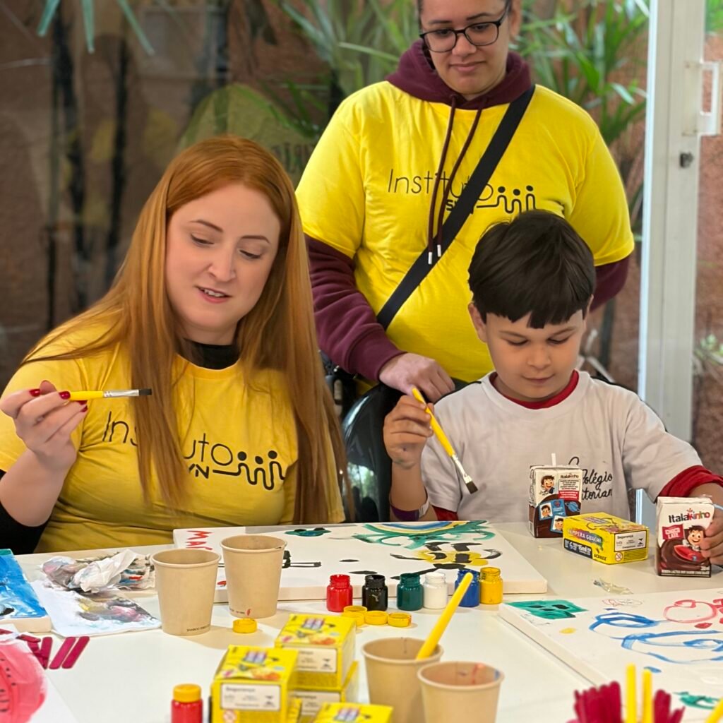 Voluntária do Instituto SYN e criança atendida pelo Instituto Nosso Olhar pintando juntas durante a ação Artista por um Dia.